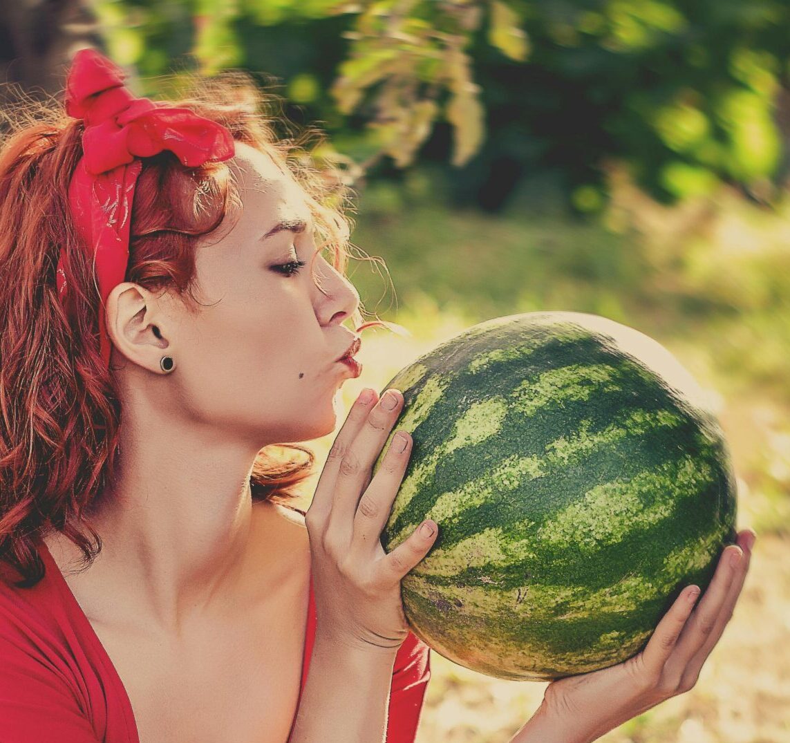 Young woman in red outfit savoring a watermelon outdoors on a sunny day.